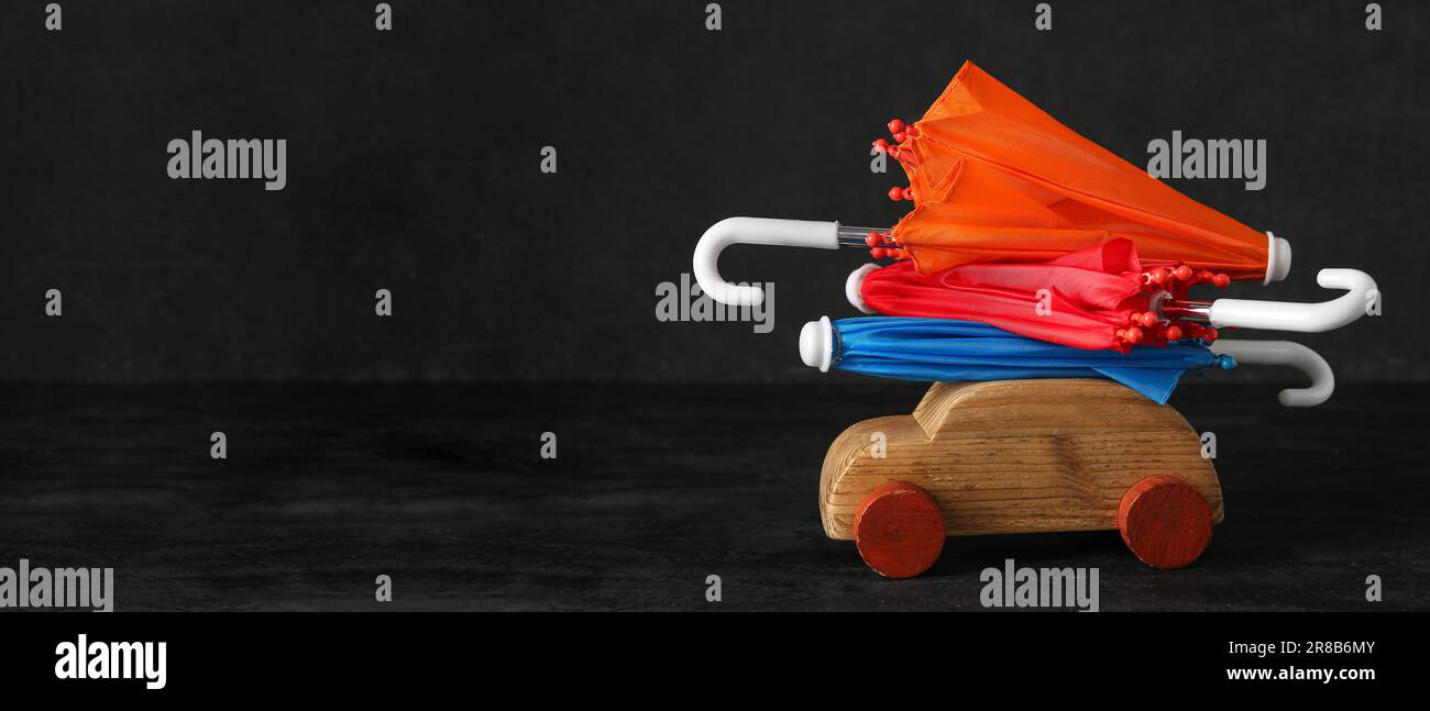 Wooden toy car and mini umbrellas on black background with space for