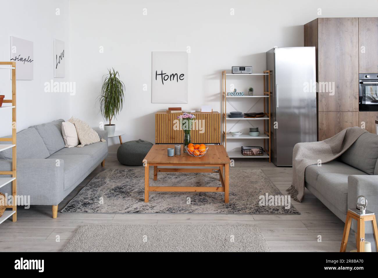 Interior of light open plan kitchen with fridge and grey sofas Stock
