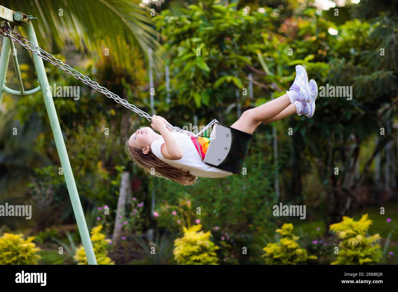 Child swinging on playground on sunny summer day in a park. Kids swing. School or kindergarten yard and play ground. Stock Photo