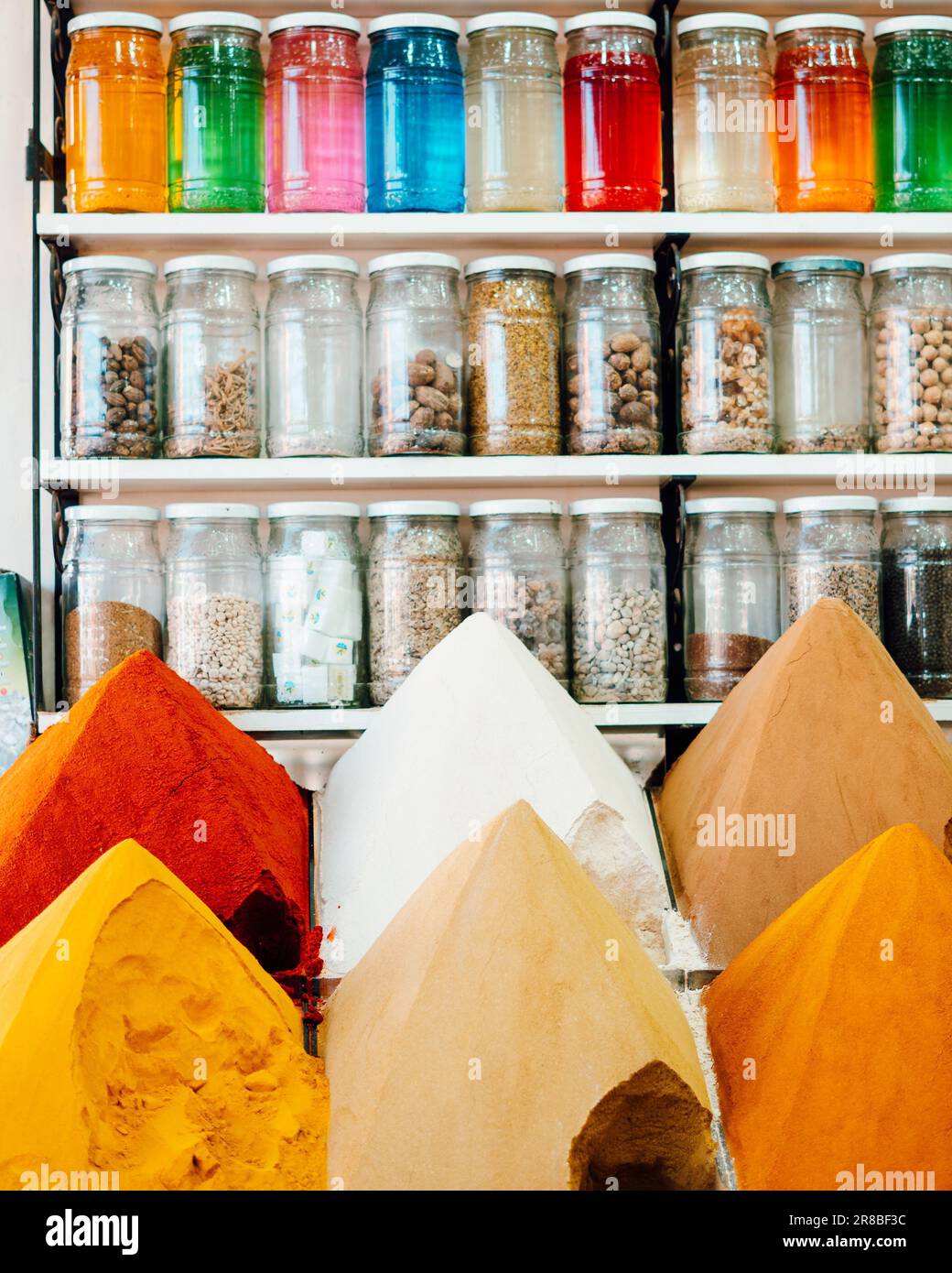 A wide variety of spices and condiments neatly arranged on a wooden shelf, with multiple glass jars in the background Stock Photo