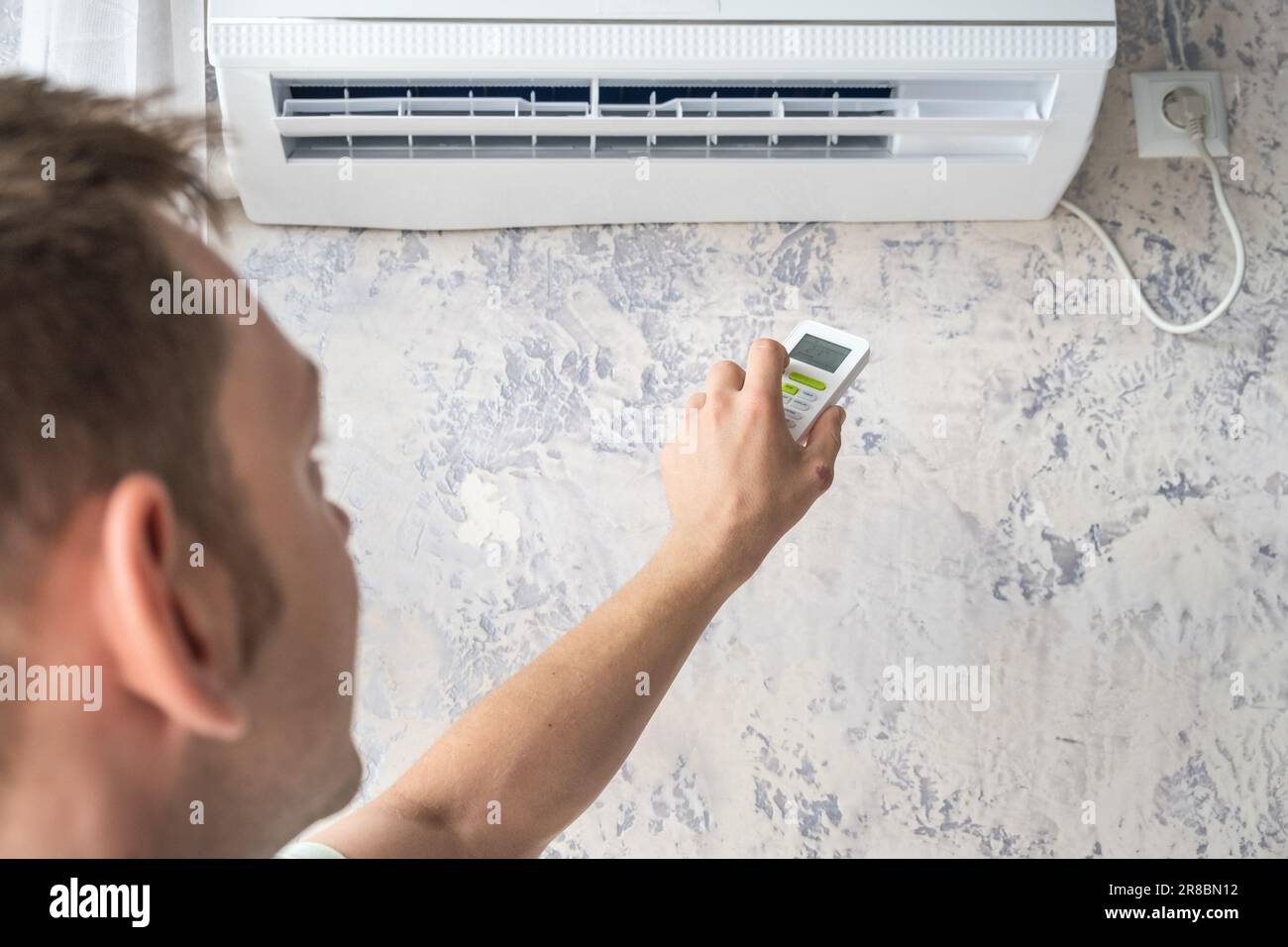Man switch on air conditioner for comfort temperature with remote controller at home in hot summer Stock Photo