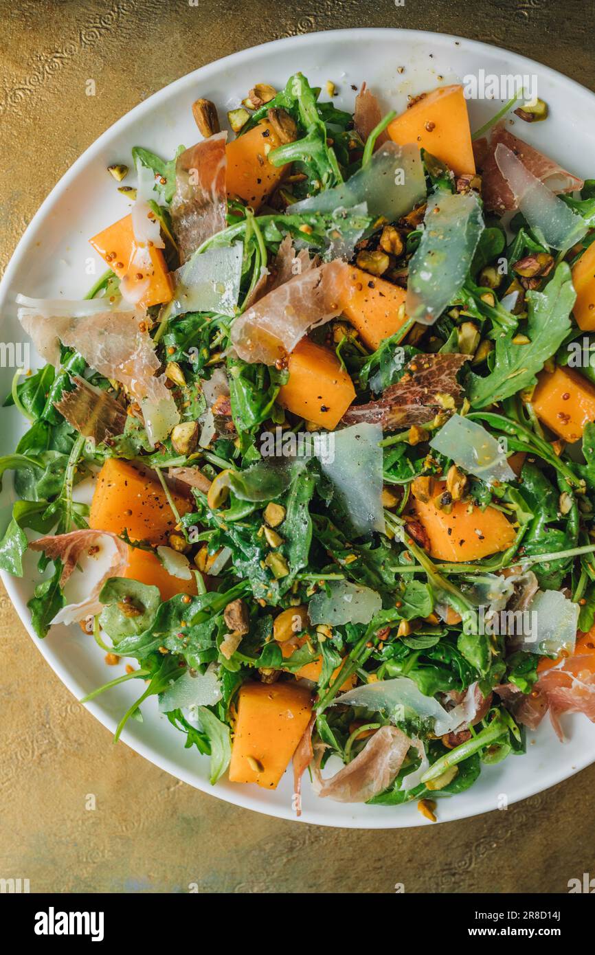 arugula salad with cheese, cantaloupe, prosciutto, pistachios on white