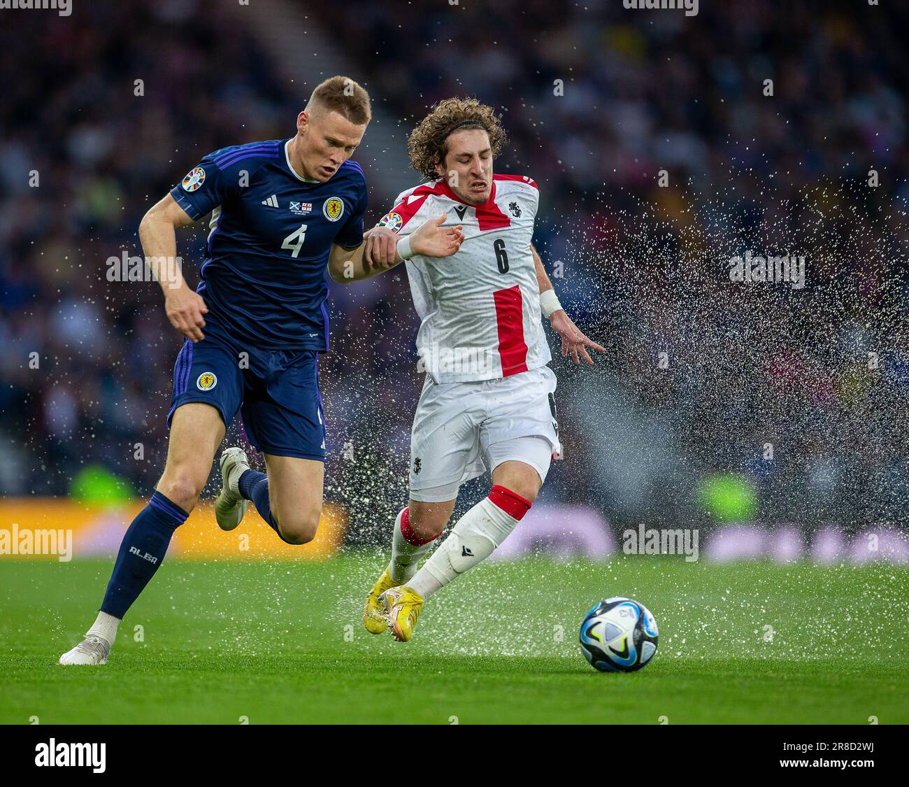 20th June 2023; Hampden Park, Glasgow, Scotland: Euro 2024 Qualifier Football, Scotland versus Georgia; Scott McTominay of Scotland and Luka Gagnidze of Georgia on the ball as water sprays up from the waterlogged pitch Stock Photo