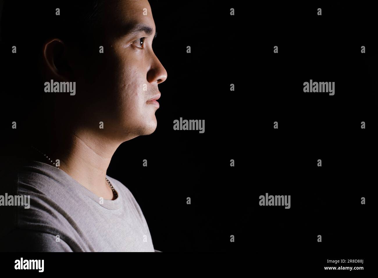 Low key and close-up shot of a young Asian man looking forward to the right side of the camera. Isolated black background. Dramatic. Stock Photo