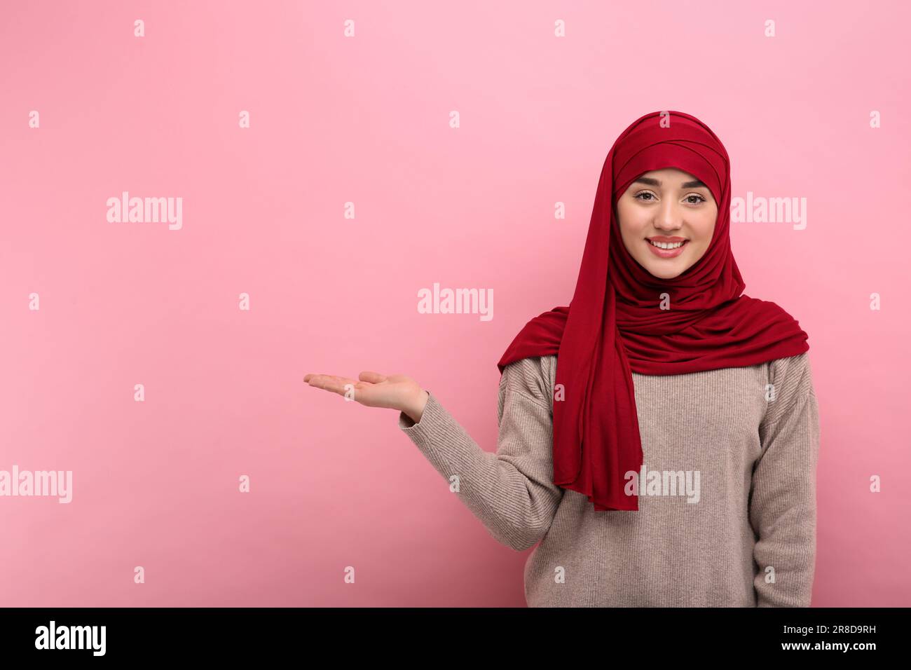 Muslim woman in hijab pointing at something on pink background, space ...