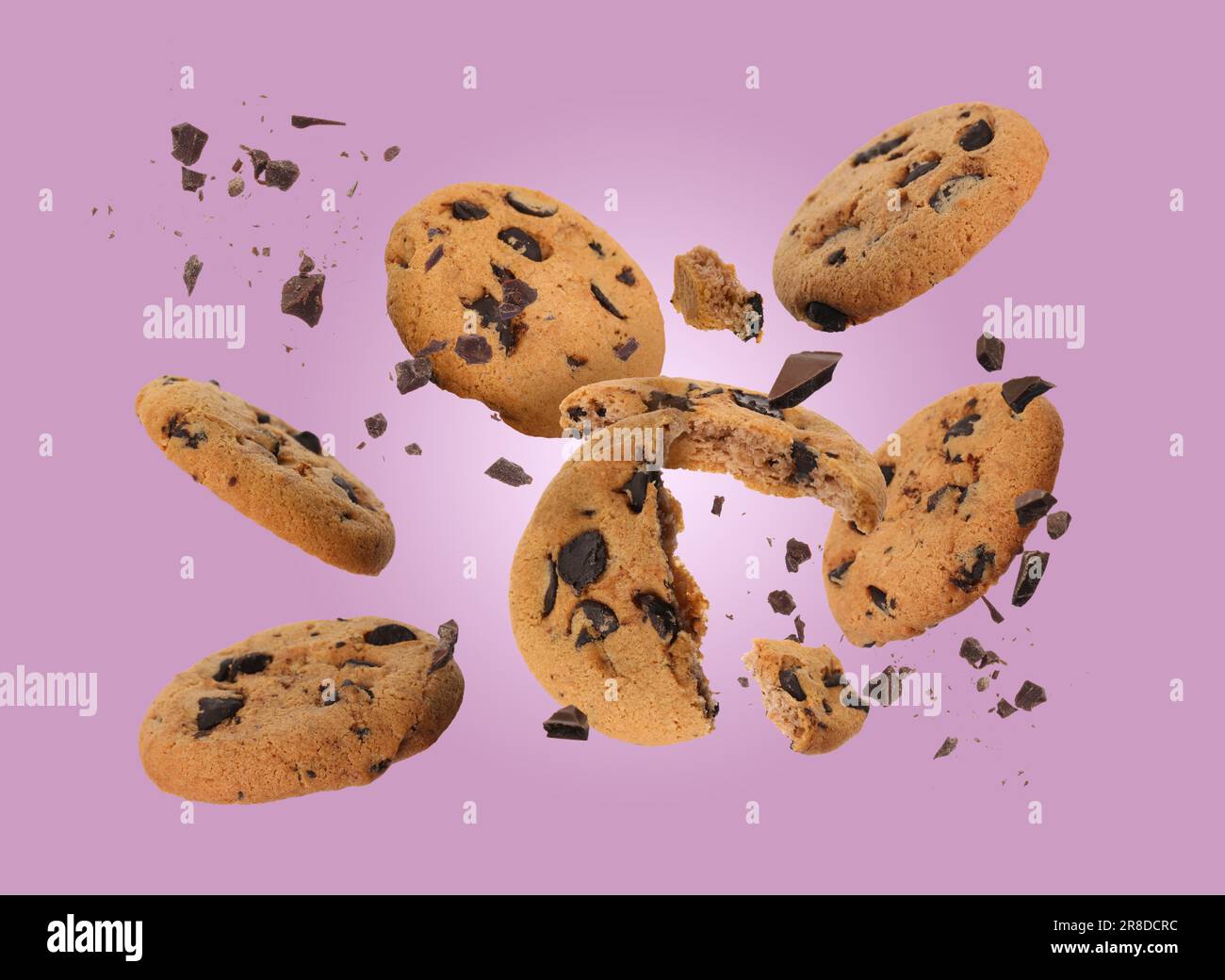 Tasty chocolate chip cookies falling on dusty pink background Stock