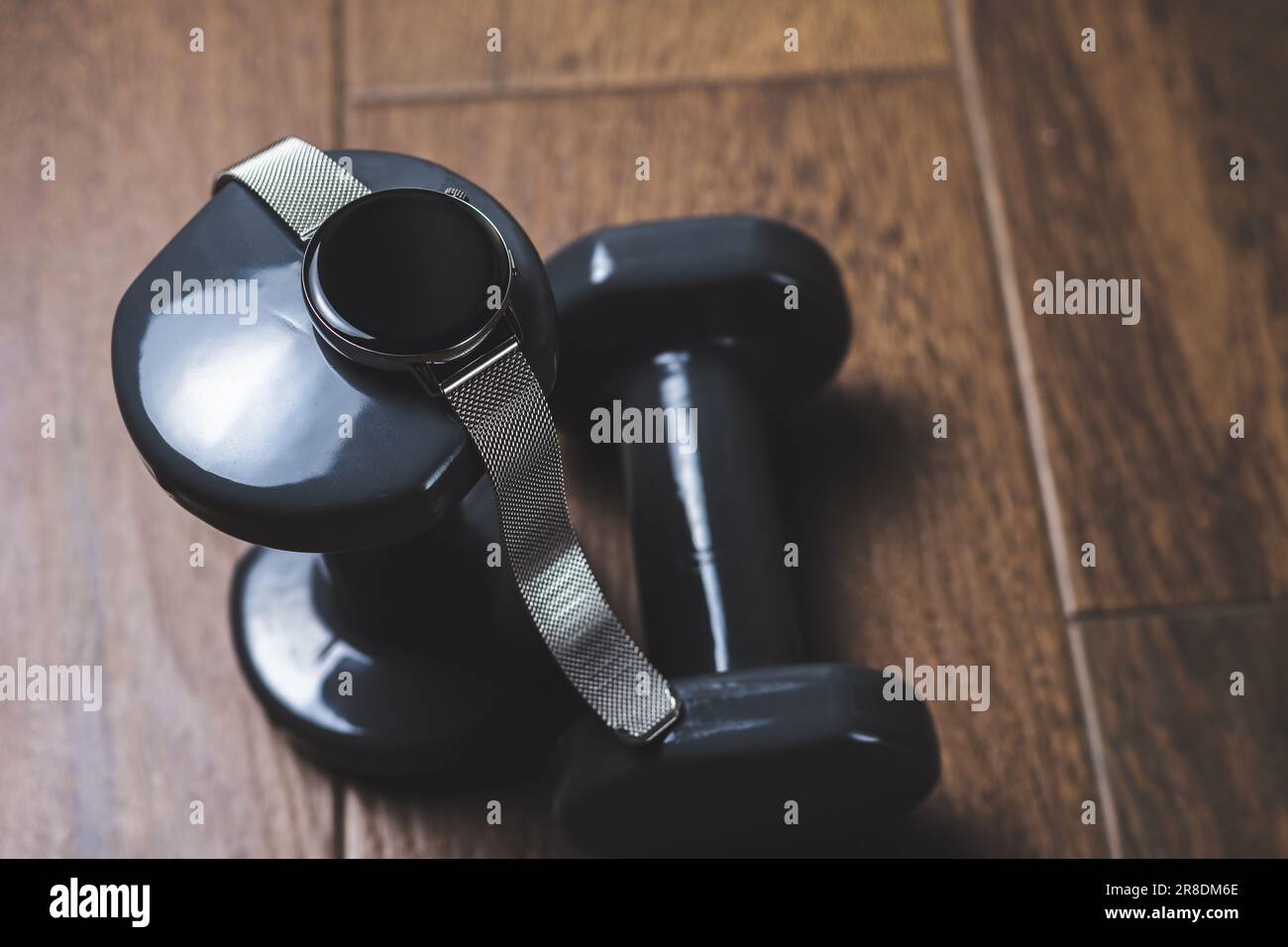 Rhythm and Determination: A smartwatch stands out on top of dumbbells placed on a wooden floor, inspiring motivation and the drive needed to achieve Stock Photo