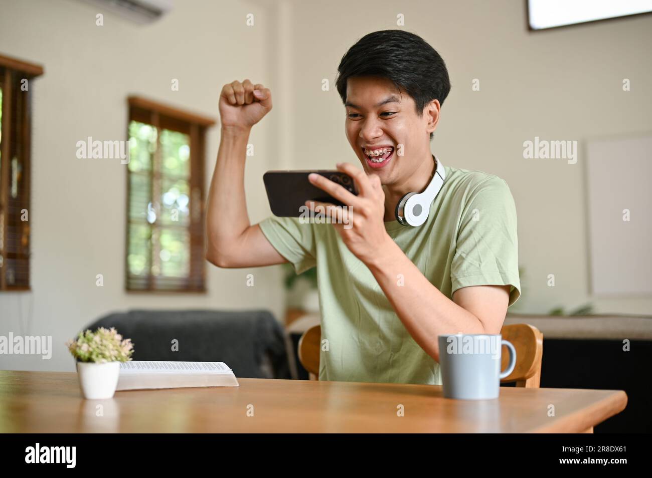 An excited and overjoyed young Asian man in comfy clothes raises his