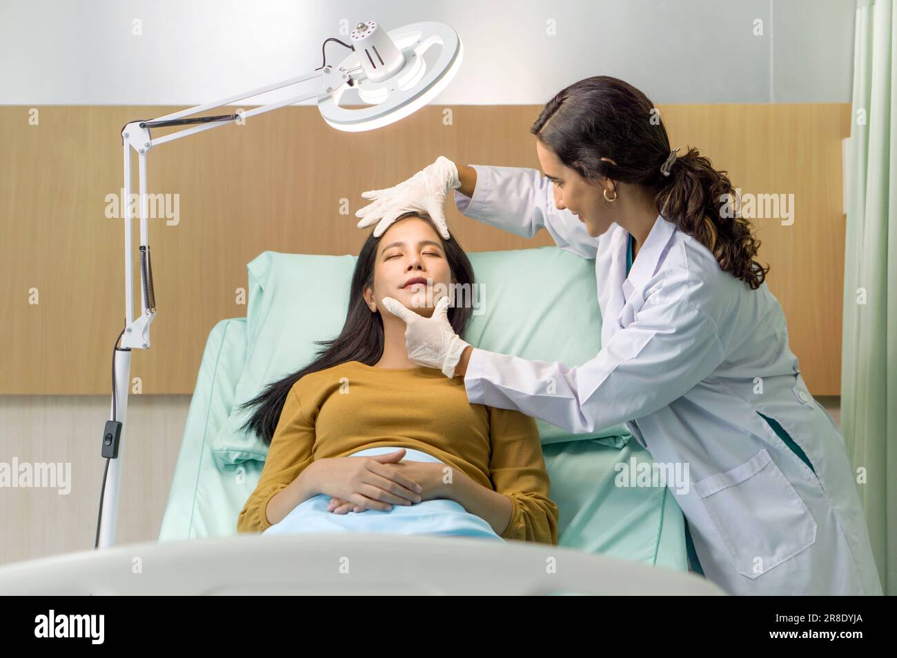 Female doctor or dermatologist  examining facial skin of young patient prepare before facelift surgery. Atmosphere at cosmetic surgery department in h Stock Photo