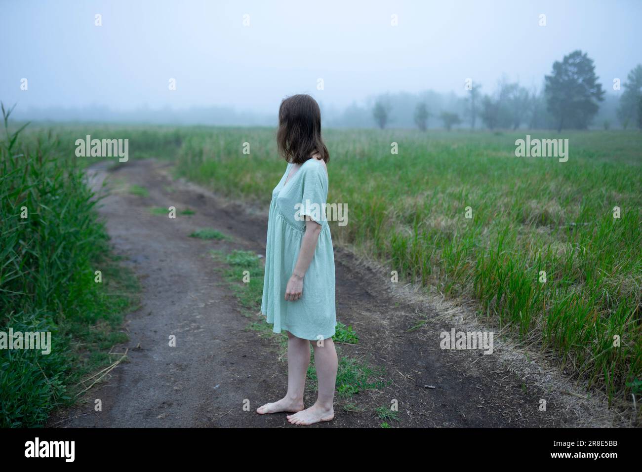 Woman standing on dirt road and looking away Stock Photo