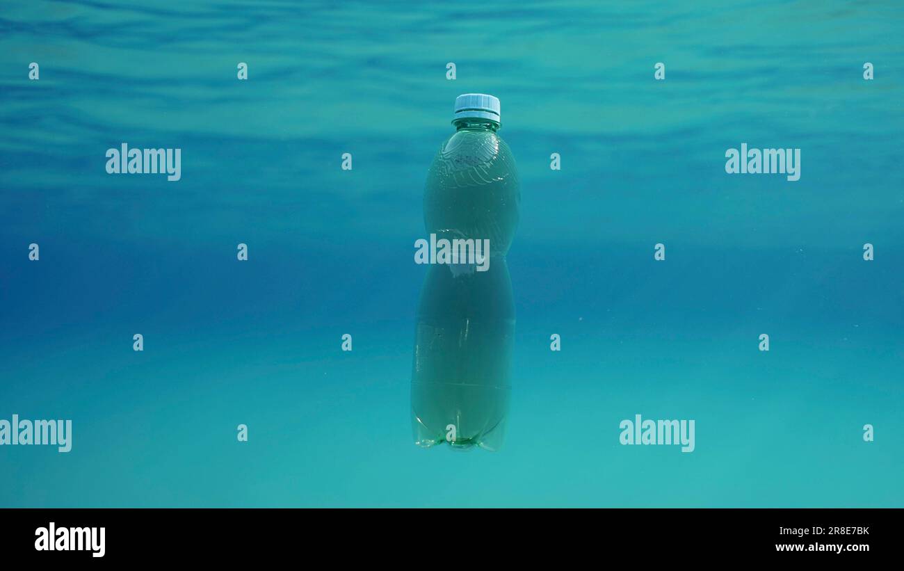 Green plastic bottle drifting under surface of blue water. Plastic
