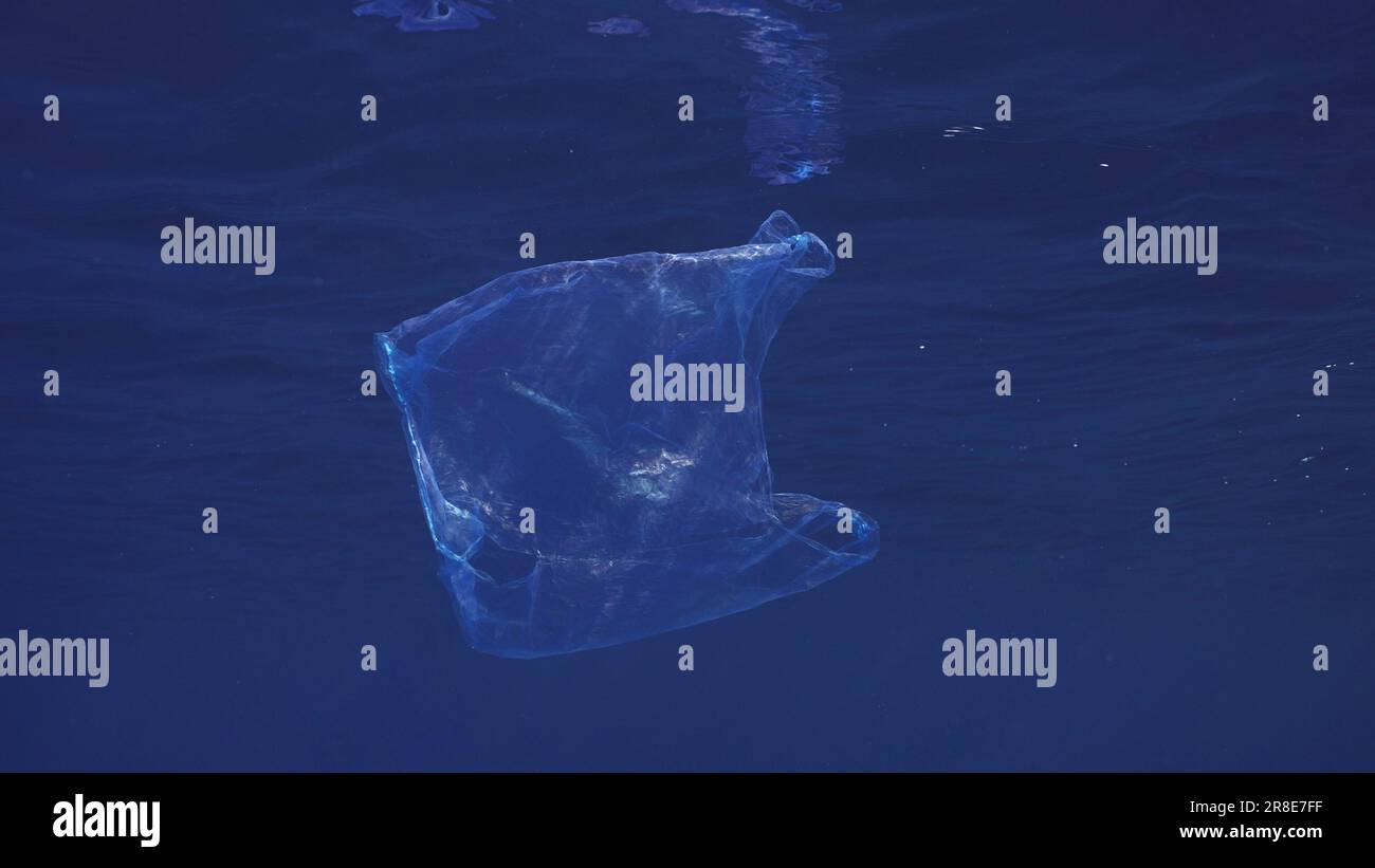 Disposable blue plastic bag floats under surface in blue water. Plastic bag thrown into sea drifts under surface of blue water in morning time, Red se Stock Photo