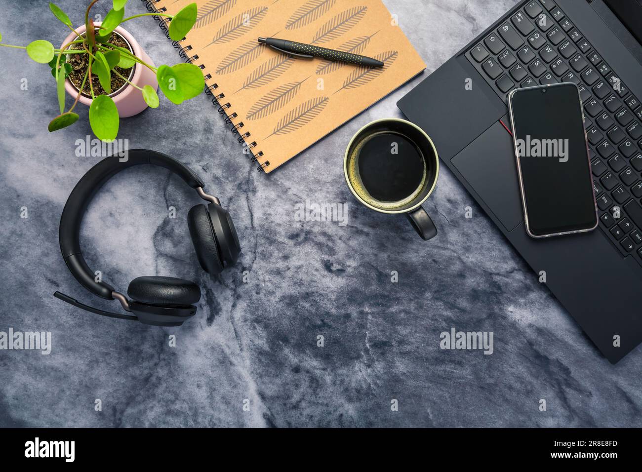 Working from home. Desk office with laptop, notepad, coffee cup,  headphones and plant Stock Photo