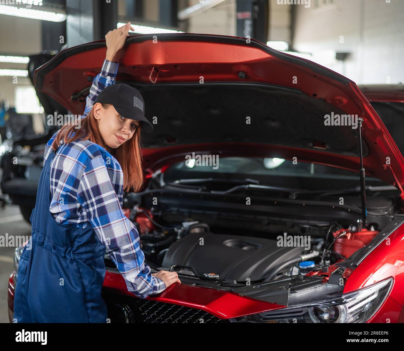 Woman auto mechanic opens the hood of a car in a car service Stock