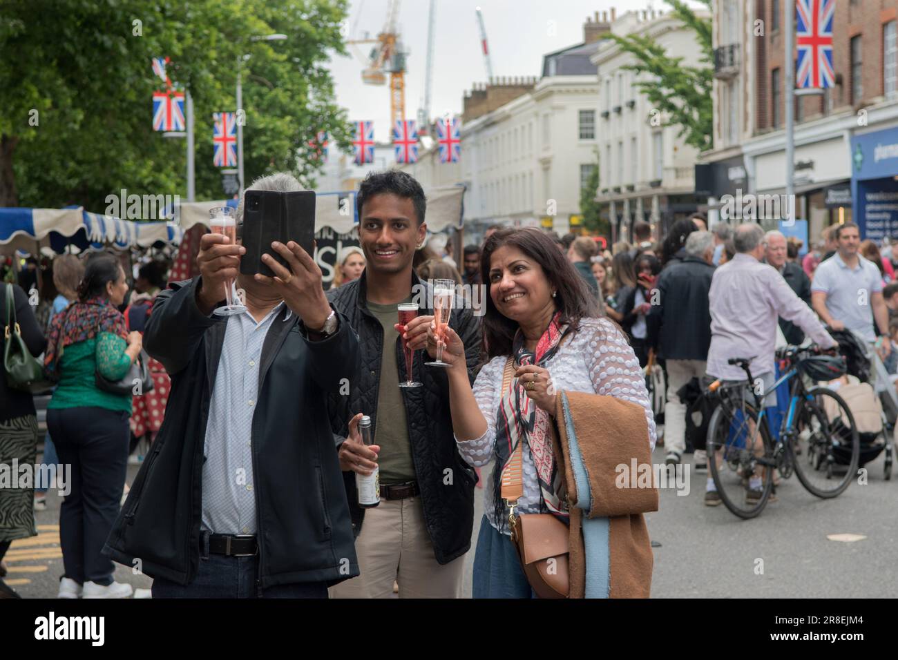 Chelsea, London, England 4th June 2022. The Kings Road, Platinum Jubilee Street Party, that is supporting the British Red Cross Ukraine crisis appeal. The Kings Road is in part closed to traffic, crowds of local and tourists enjoy the summer weather. A family from Asia take a selfie holding plastic Champagne picnic glasses. Stock Photo