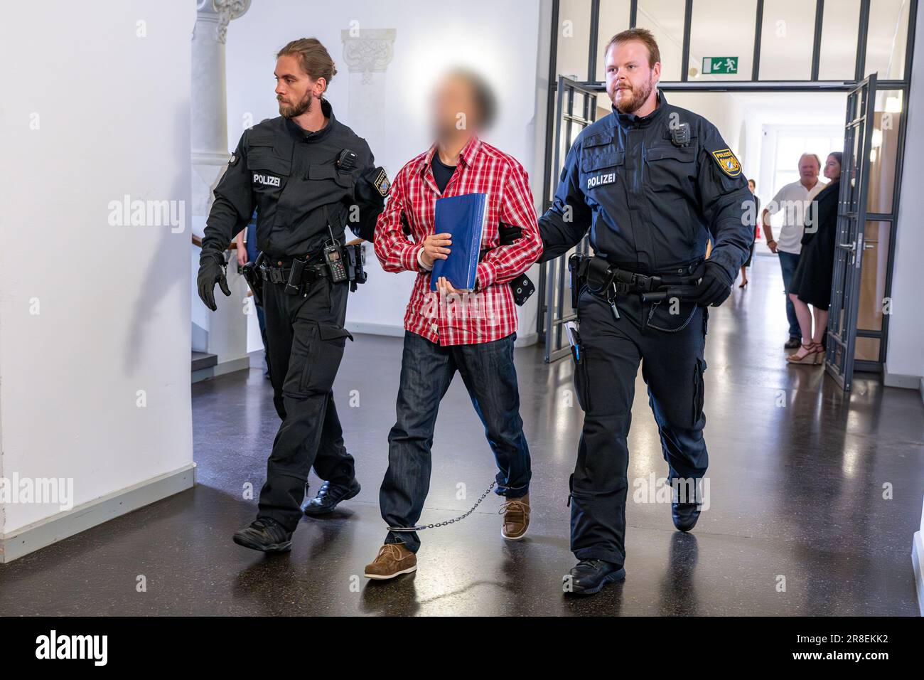 Regensburg, Germany. 21st June, 2023. The defendant (M) is led to the courtroom in shackles by police officers because of an appeal. With a jump out of the window of the Regensburg District Court, the man sentenced to life imprisonment for the murder of a 76-year-old woman in Nuremberg in 2011 had caused an international police operation in January. Credit: Armin Weigel/dpa - ATTENTION: The defendant has been pixelated on the instructions of the lawyer for legal reasons/dpa/Alamy Live News Stock Photo