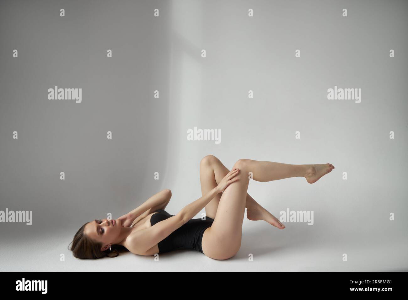 Sexy woman lying on the floor in a black bodysuit, studio portrait. Perfect body the figure of a young woman Stock Photo