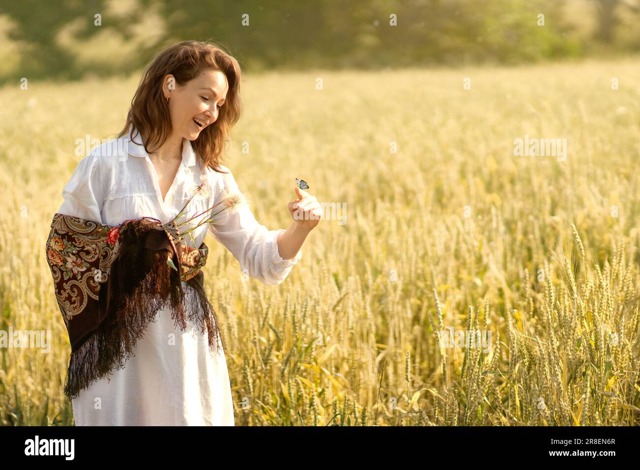 a young white woman went for a walk in a wheat field in the early summer morning,  a blue butterfly landed on her finger, the girl was very surprised. Stock Photo
