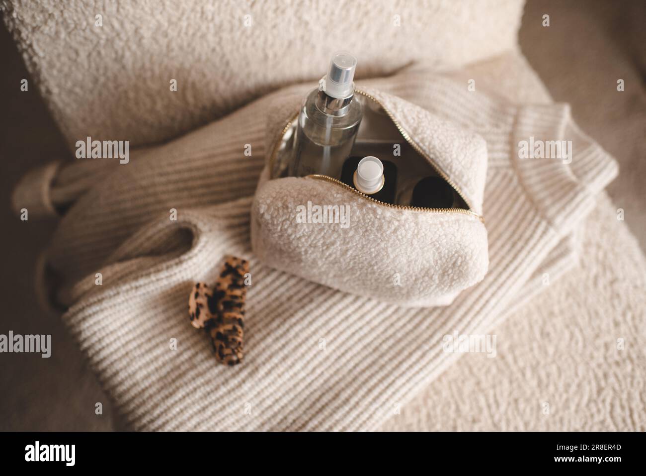 Fluffy cosmetic bag with make up cosmetic products on knitted clothes in chair closeup top view. Stock Photo