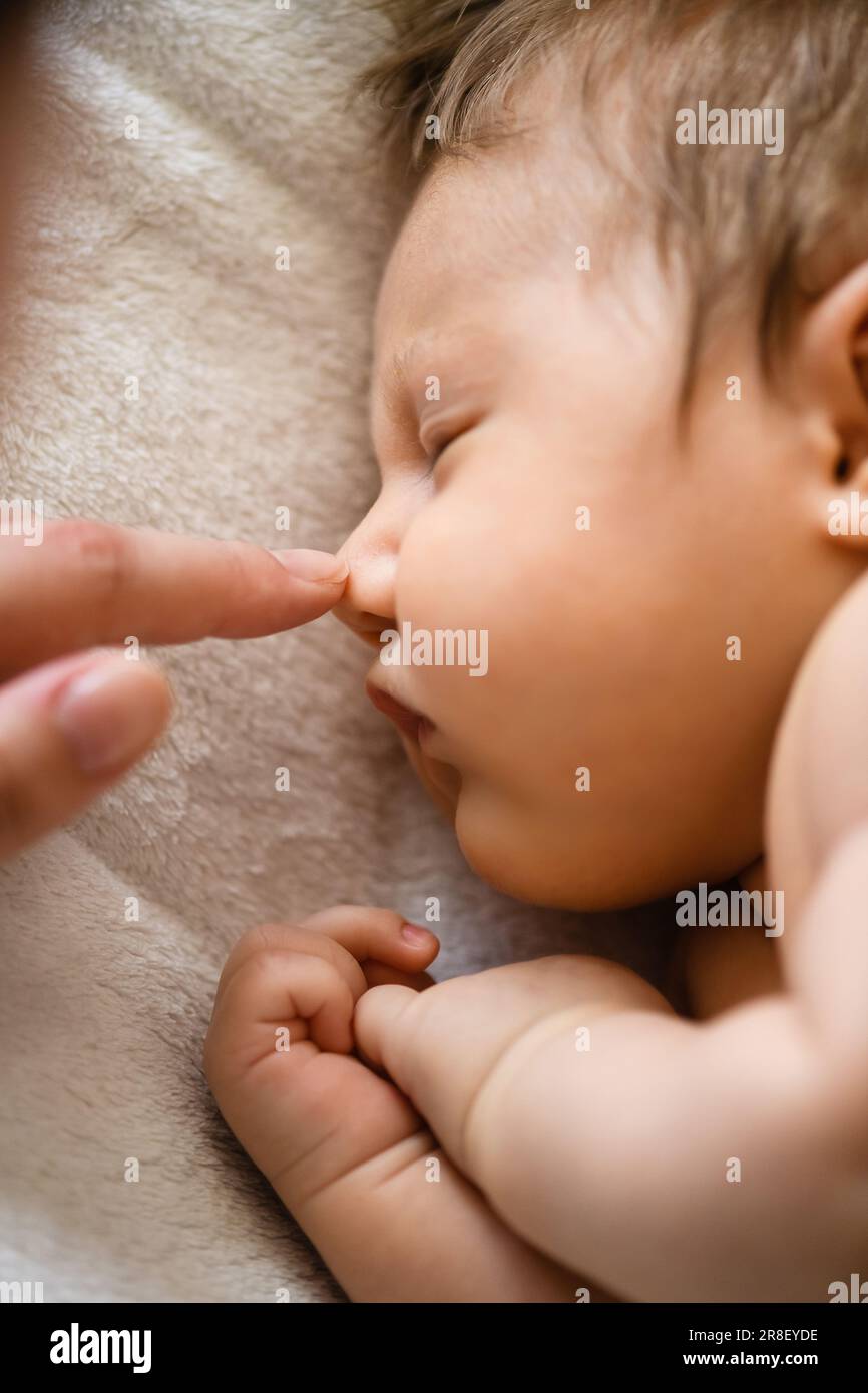 Mother finger touch newborn baby tiny nose, sleeping in bed crib adorable infant, family love close up Stock Photo