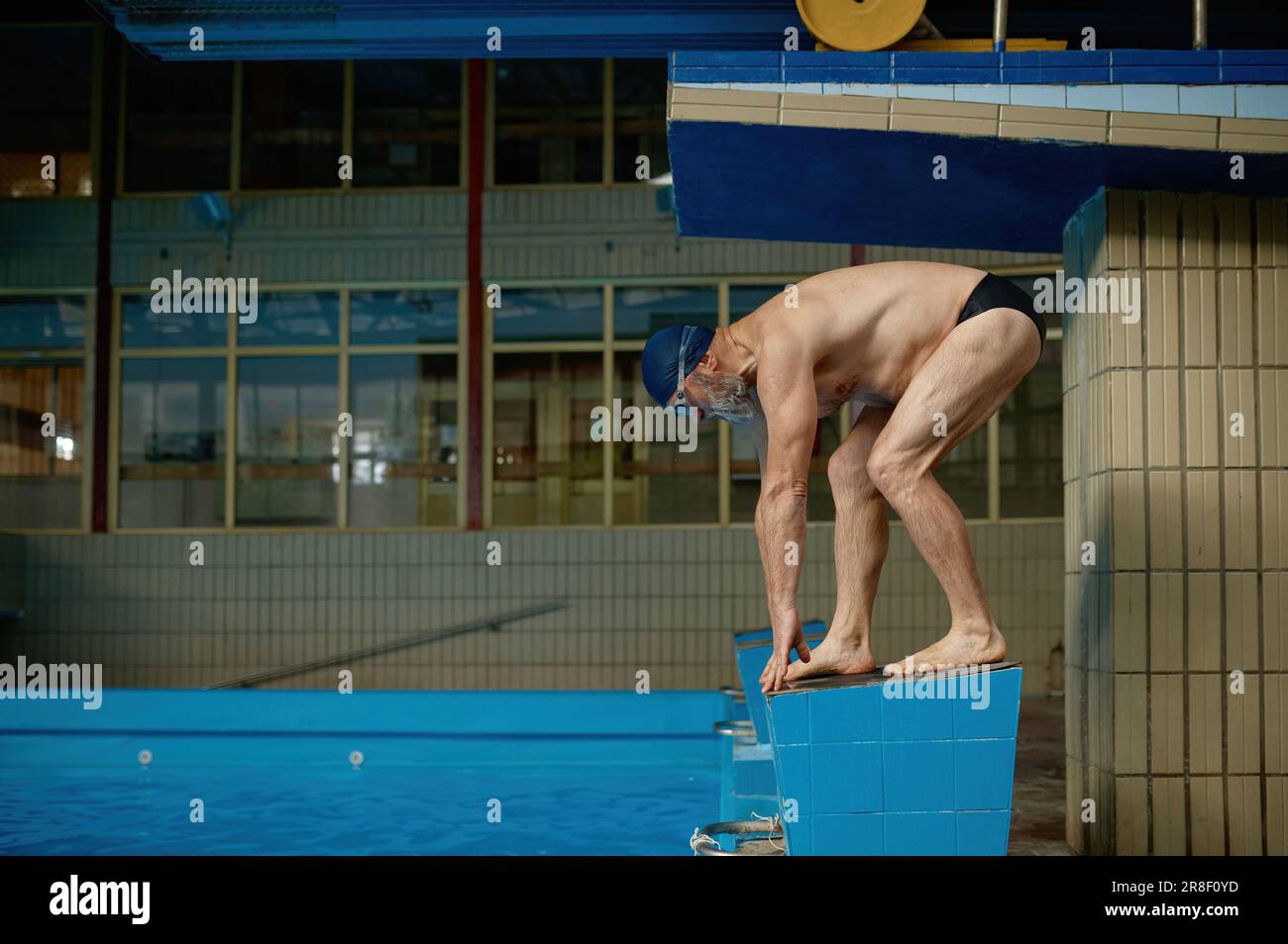 Senior man athlete standing on starting block preparing to jump in pool Stock Photo