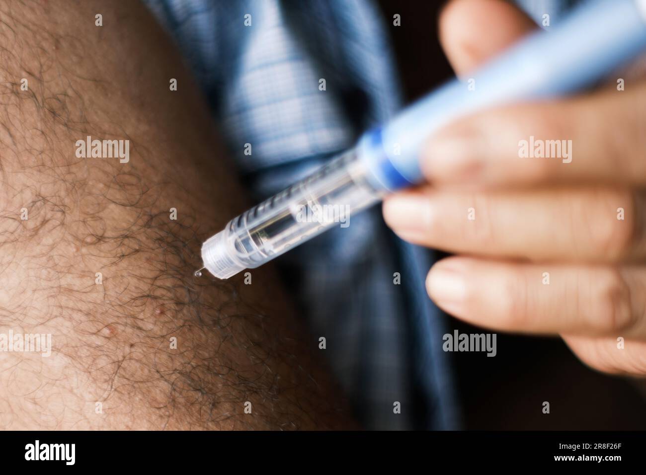 Close-up image of a brunette man self-administering an insulin injection. The needle tip, glistening with a bead of insulin, is a potent symbol of the Stock Photo