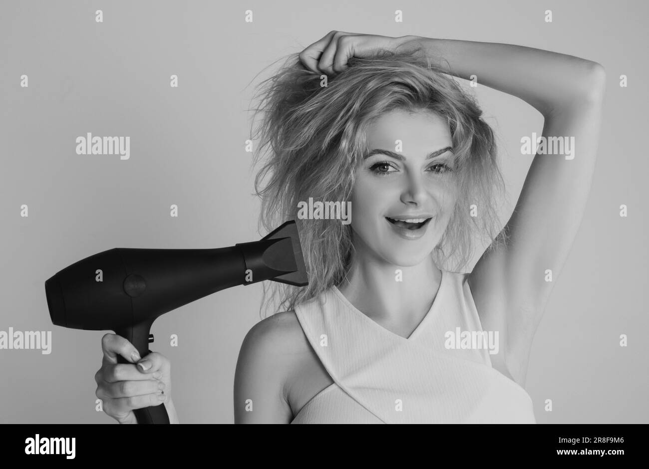 Health hair and beauty concept. Girl with blonde hair using hairdryer. Young attractive happy laughing blonde woman with hair dryer. Hairstyle Stock Photo