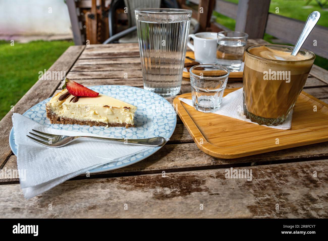 Cheesecake, two coffee and water on wooden table in garden. Stock Photo