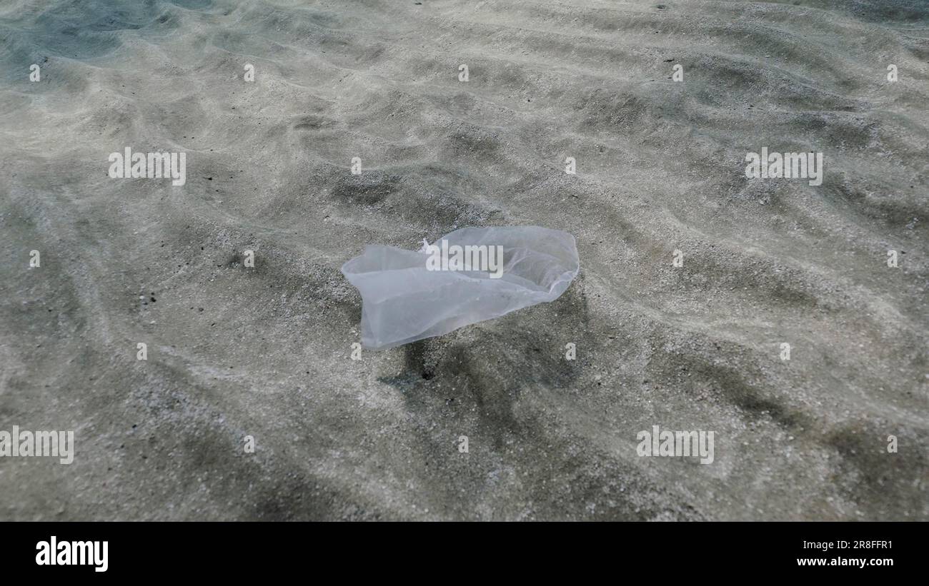 Plastic pollution, white plastic bag moves slowly in stream of water over sandy bottom Close up of sandy bottom in shallow water with plastic bag Stock Photo