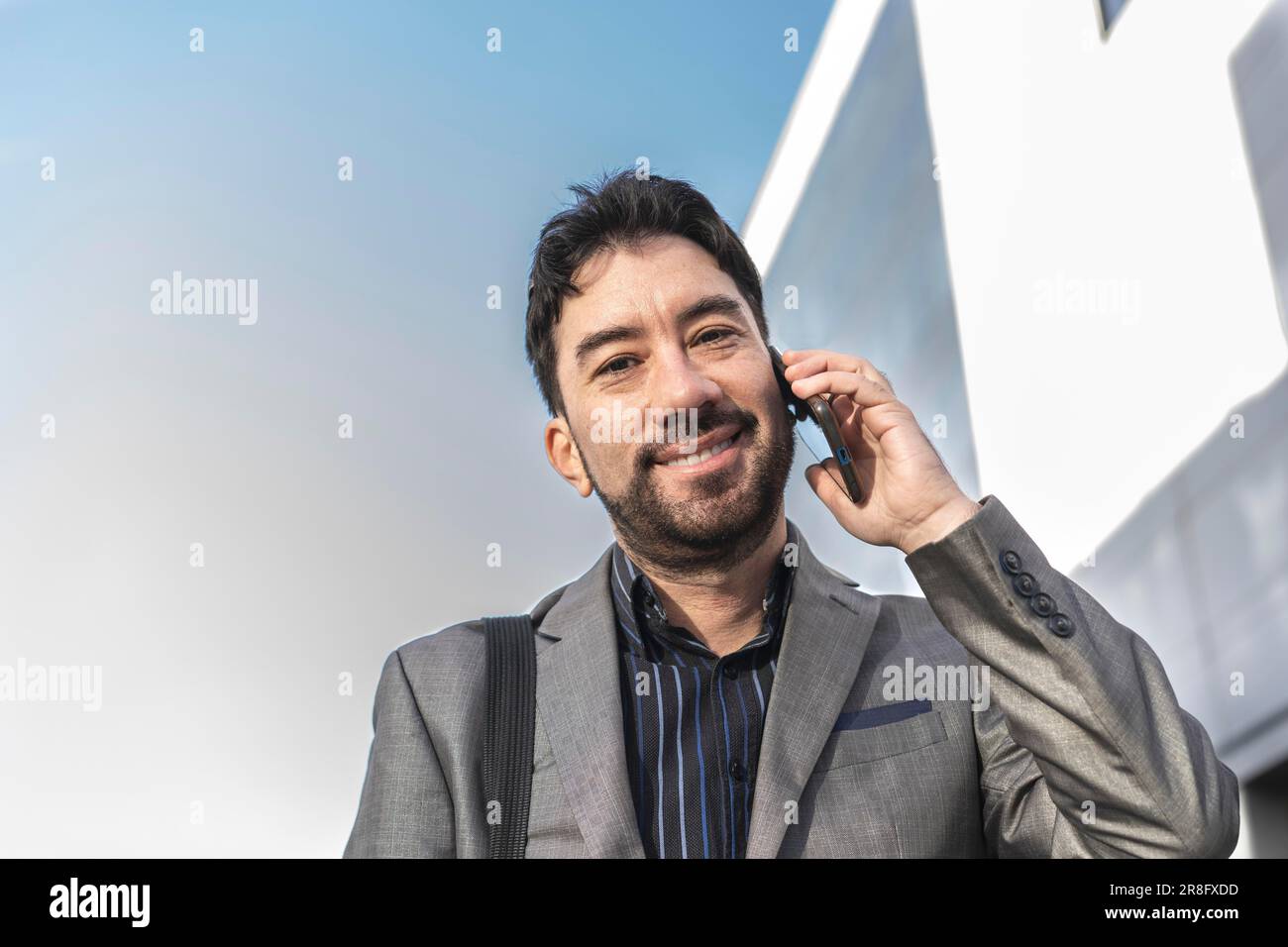 Low-angle view of an attractive businessman talking on the cell phone while looking at camera in the street Stock Photo