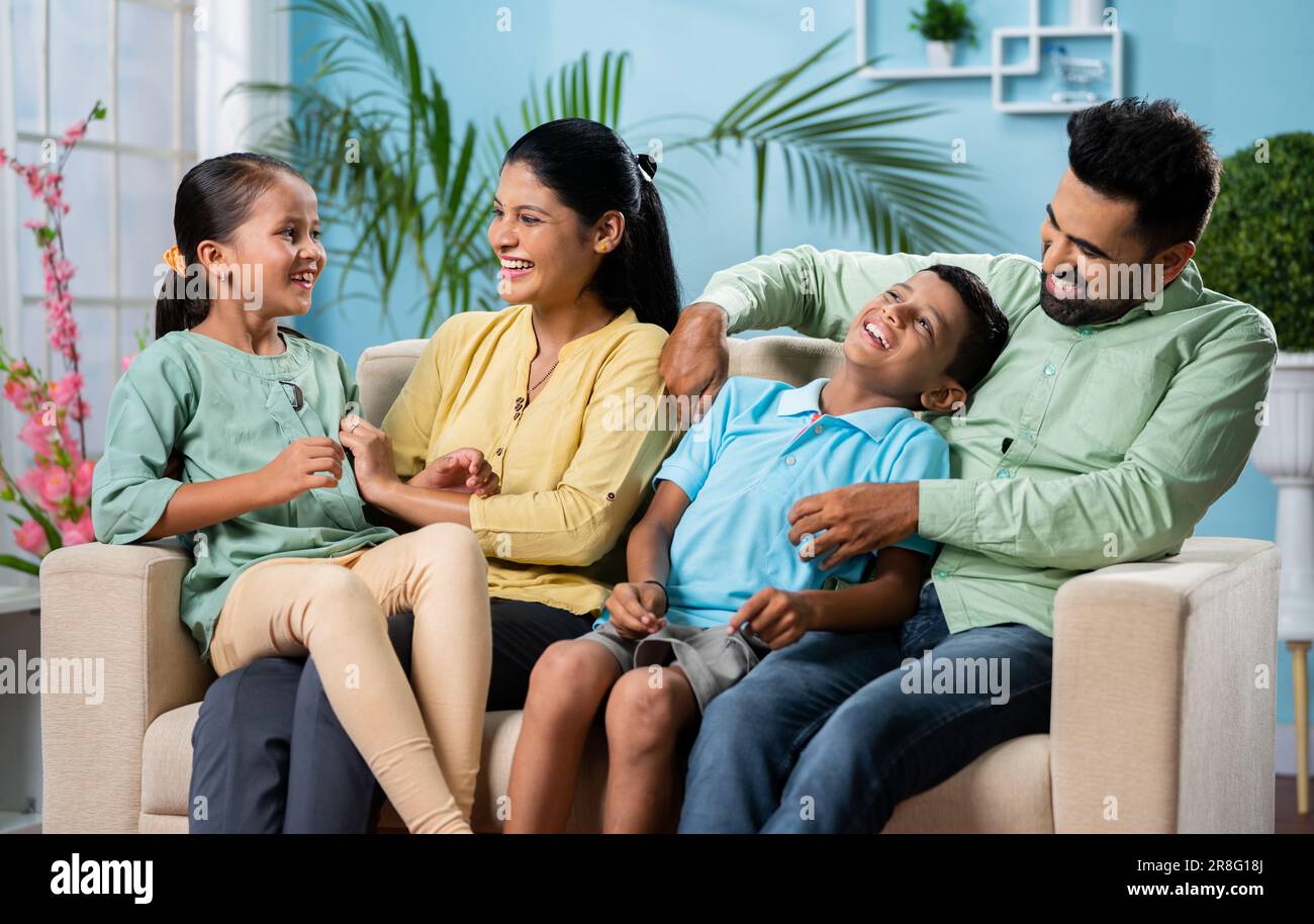 focus on mother, Happy Indian couple with kids playing by cuddling or tickling together while sitting on sofa at home - concept of family bonding Stock Photo