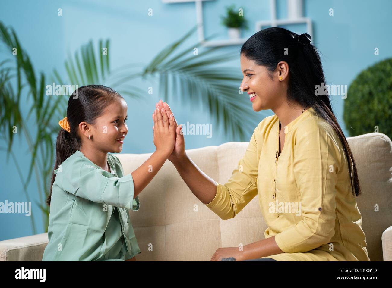 focus on kid, Happy Indian mother playing with daughter while sitting on sofa at home - concept of family time, weekend holydays and playful childhood Stock Photo