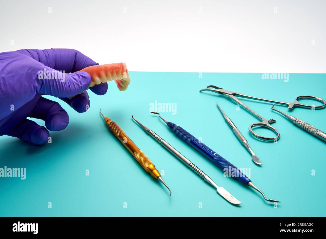 A dental technician picks up a denture from a workbench with various
