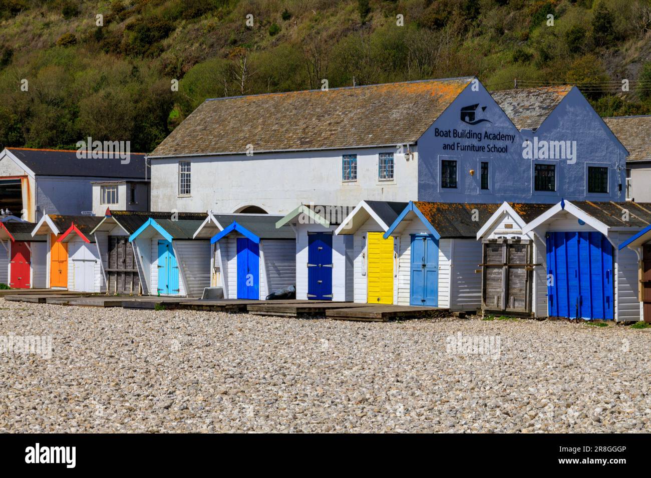 Colourful beach huts in front of the Boat Building Academy and Furniture School in Lyme Regis on the Jurassic Coast, Dorset, England, UK Stock Photo