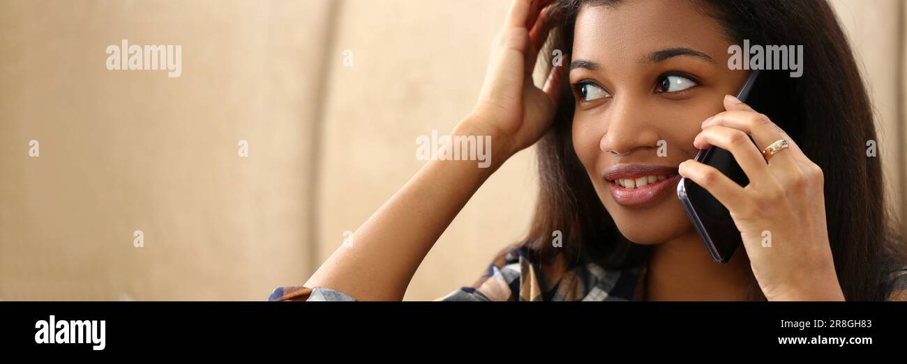 Smiling pensive young black woman talking on phone in living room Stock ...