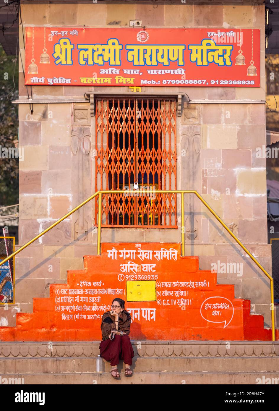 Varanasi, Uttar Pradesh, India - March 05 2023: Portrait of foreigner woman sitting on stairs of temple at assi ghat during morning. Stock Photo