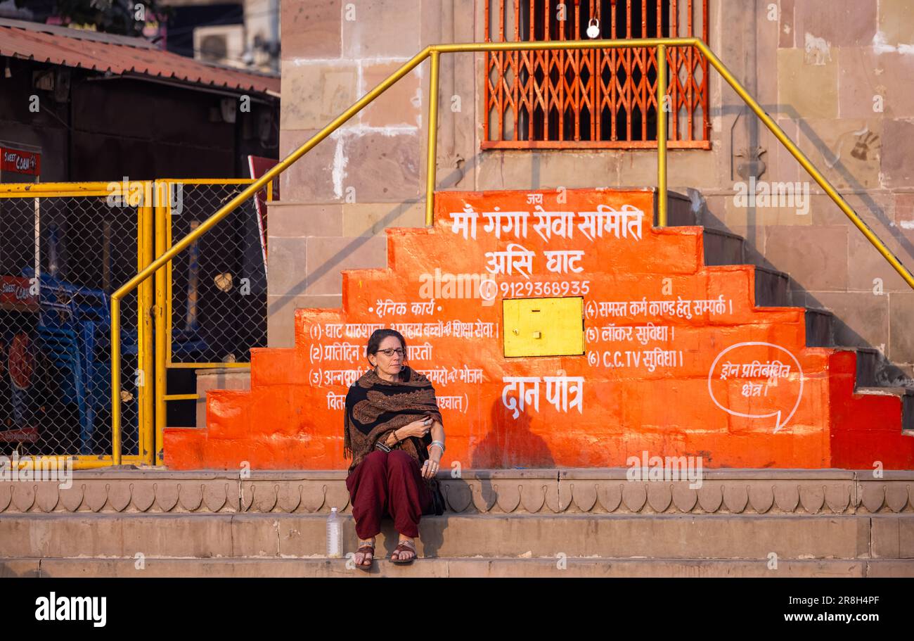 Varanasi, Uttar Pradesh, India - March 05 2023: Portrait of foreigner woman sitting on stairs of temple at assi ghat during morning. Stock Photo