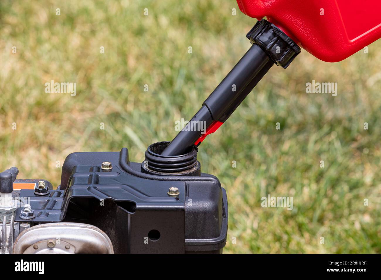Gas can pouring gasoline into fuel tank of lawnmower. Lawn equipment maintenance, service and safety concept. Stock Photo