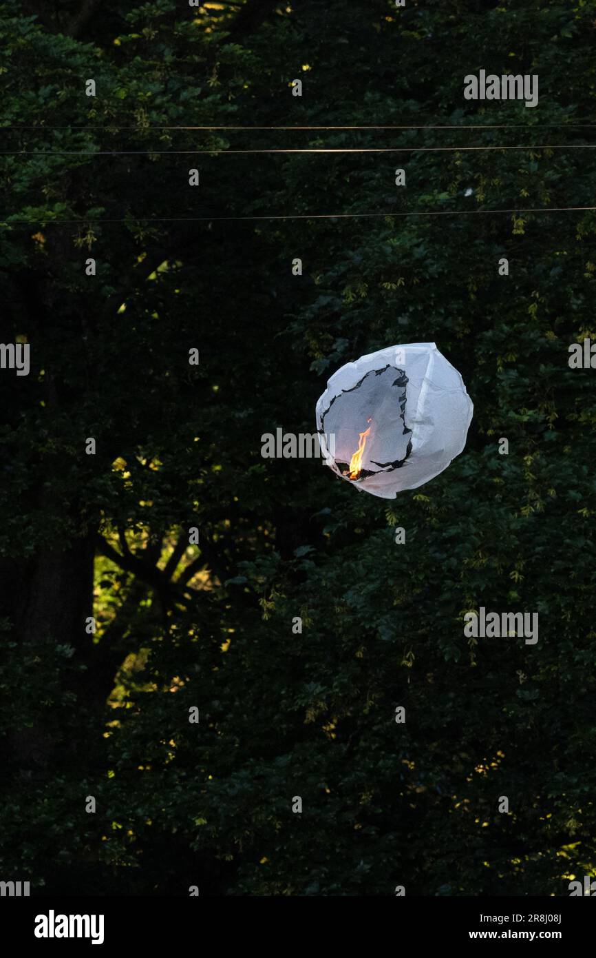 Sky lantern or Chinese lantern alight in the sky - the paper lantern has caught fire and descending next to a tree creating a fire hazard  - UK Stock Photo