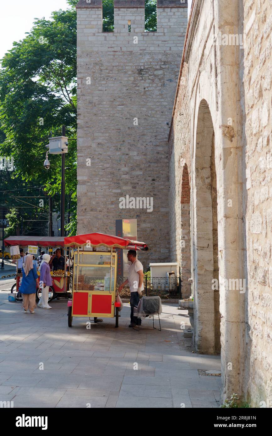 Red Cart selling Simits aka Turkish Bagels by the stone built fortress style entrance Gulhane Park in Istanbul Turkey Stock Photo