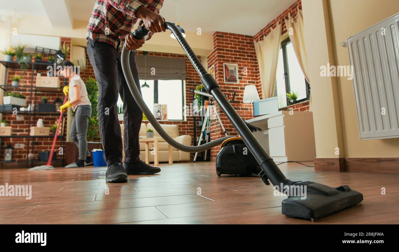 African american man vacuuming floors in living room, cleaning