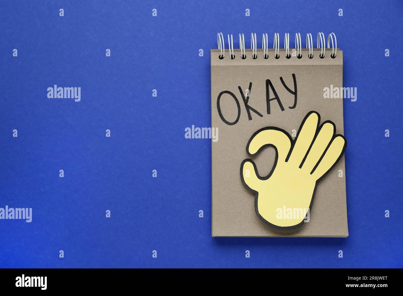 Notepad with word Okay and paper cutout of OK hand gesture on blue background, top view. Space for text Stock Photo