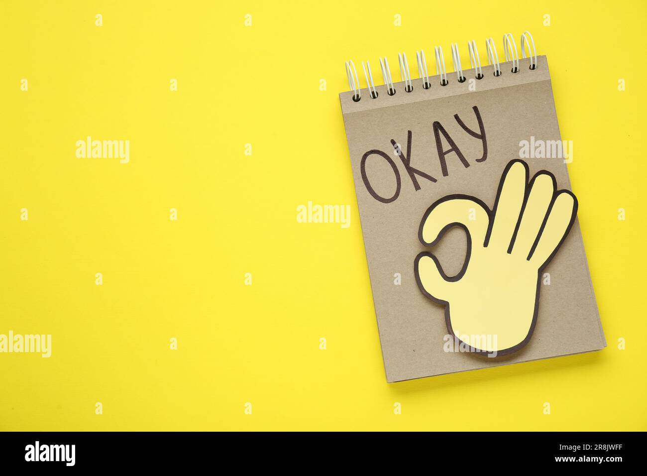 Notepad with word Okay and paper cutout of OK hand gesture on yellow background, top view. Space for text Stock Photo