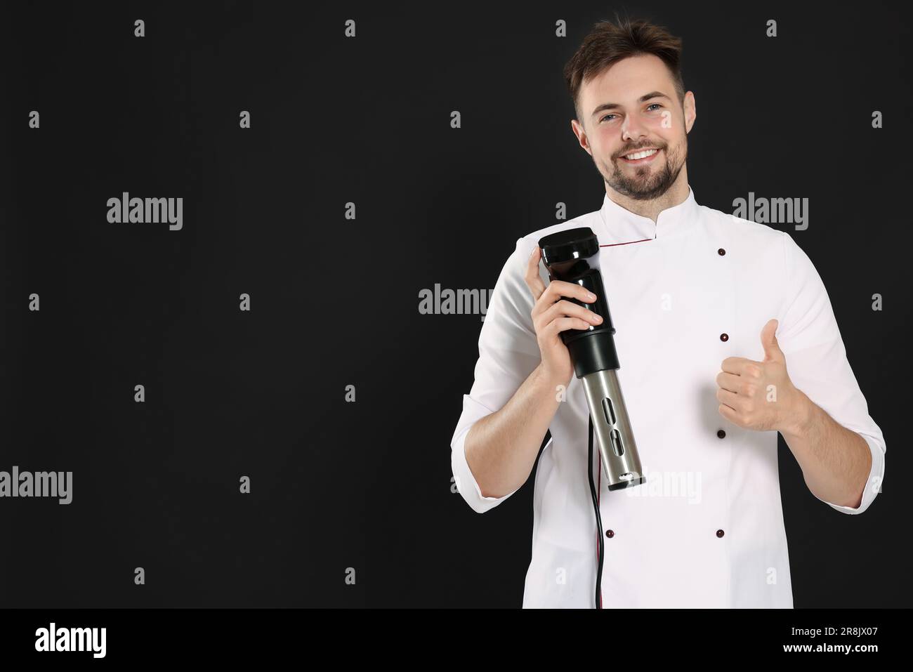 Smiling chef holding sous vide cooker and showing thumb up on black ...