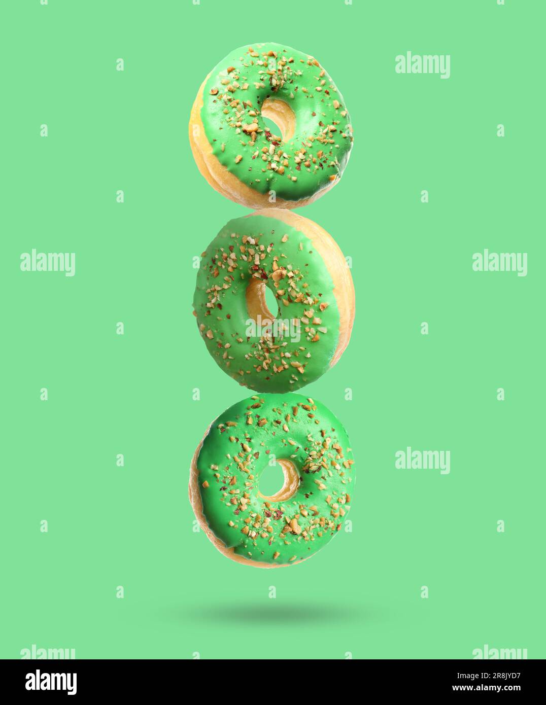 Tasty donuts with sprinkles falling on light green background Stock Photo
