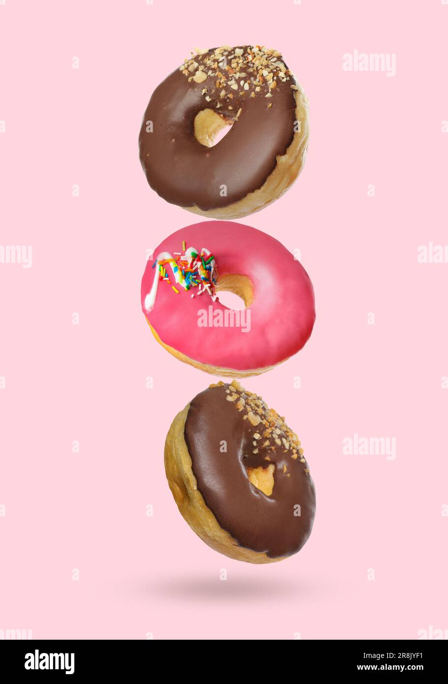 Different tasty donuts falling on pastel pink background Stock Photo