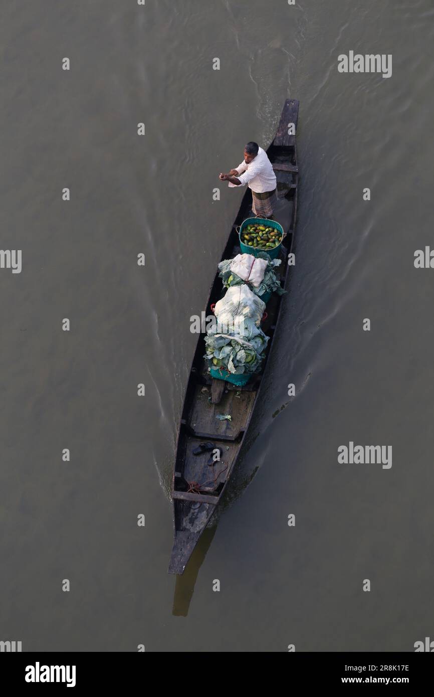 A villager transports his vegetables on a boat along a river to sell them to a market in the winter season in Bandarban, Bangladesh on February 6, 2023. Stock Photo