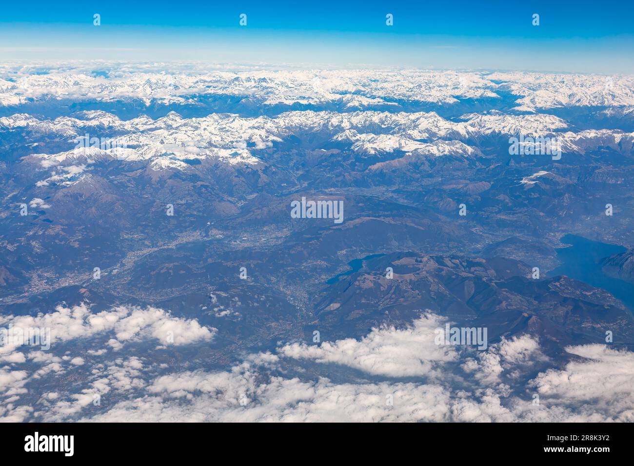 Aerial view of mountain range with snowy peaks . Clouds and blue sky as seen through window of an aircraft Stock Photo