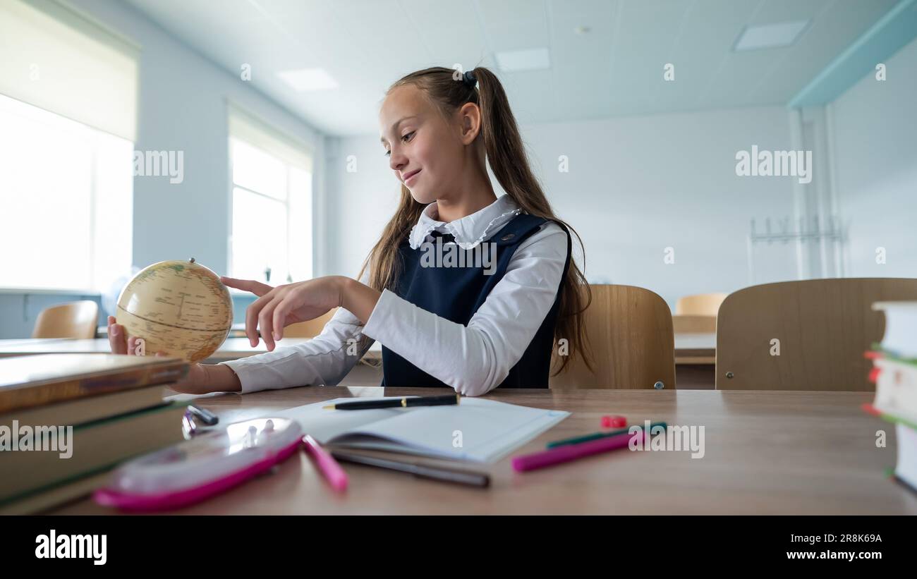 Caucasian schoolgirl sits at her desk at school and studies the globe ...