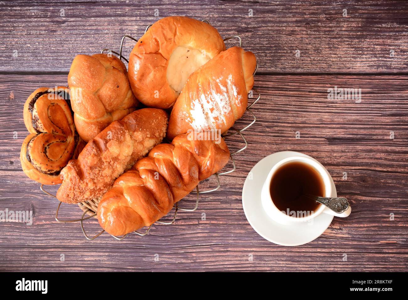 Wooden dark table with a cup of hot tea and a wicker basket with a variety of pastries. Top view, flat lay. Stock Photo